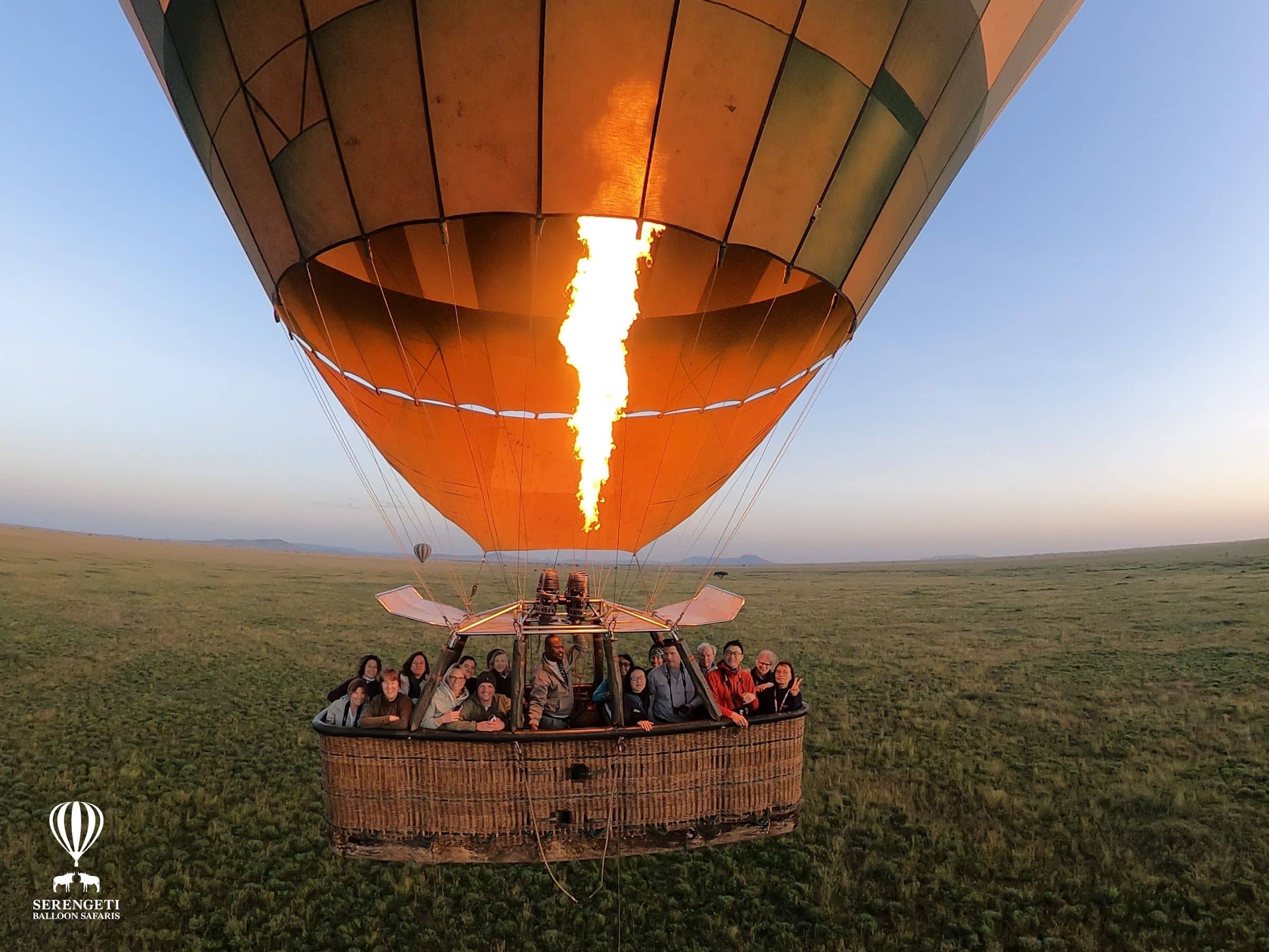 A hot air balloon basket of guests lifting off over the Serengeti plains at sunrise