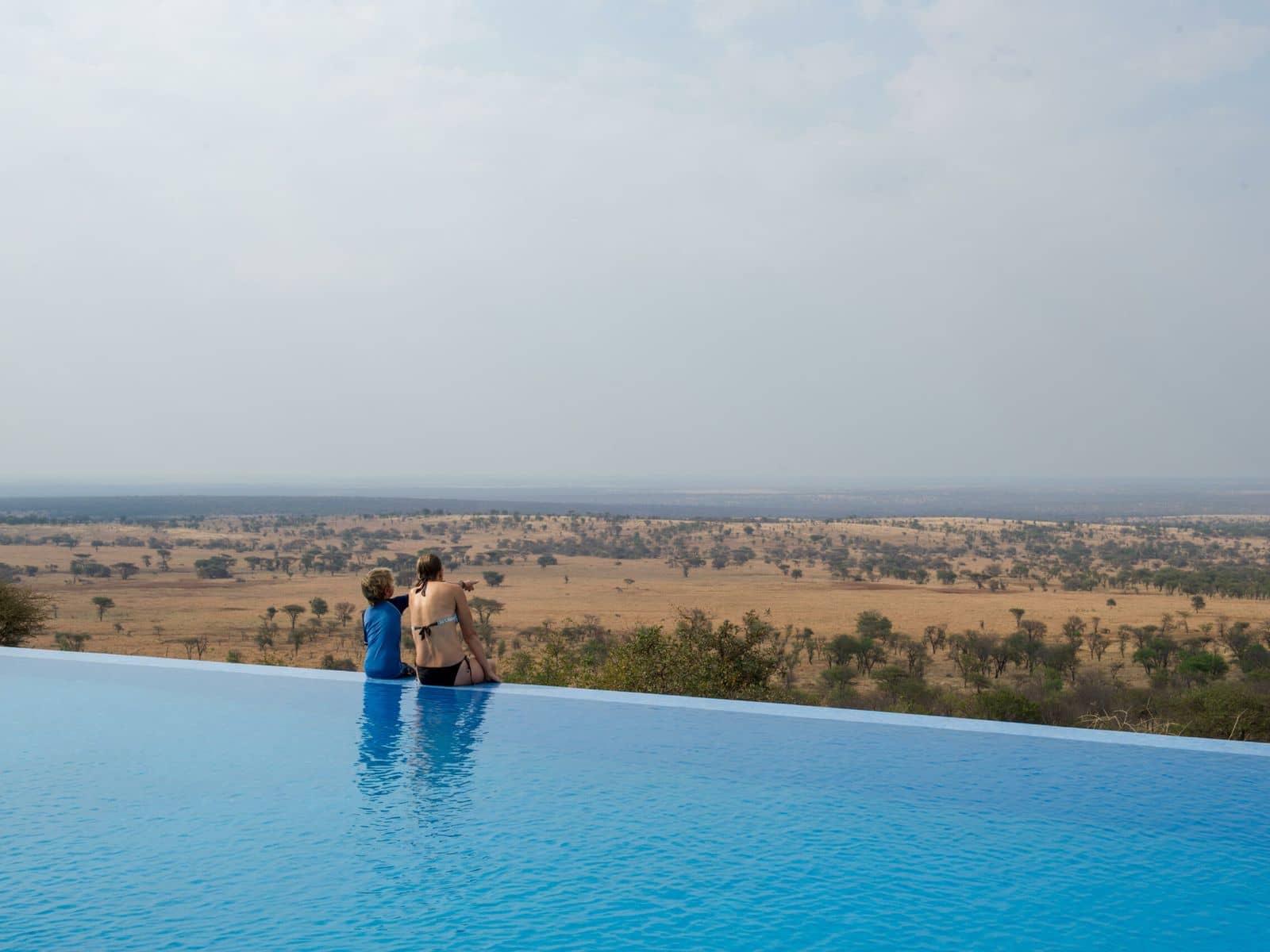 Guests at the edge of the Kubu Kubu infinity pool, looking out over the Serengeti plains