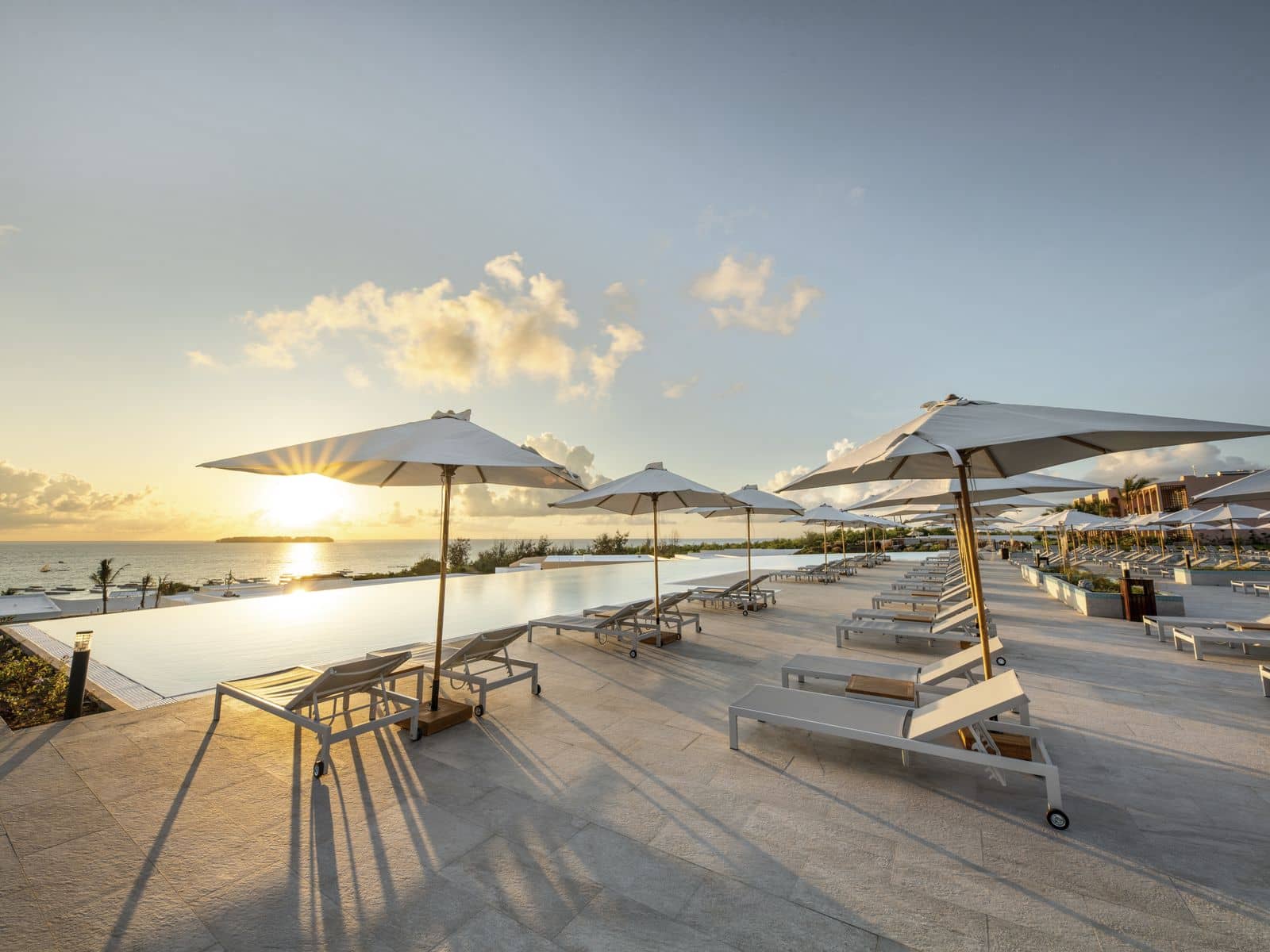The infinity pool and sun loungers of The Mora looking out to the Indian Ocean at sunset