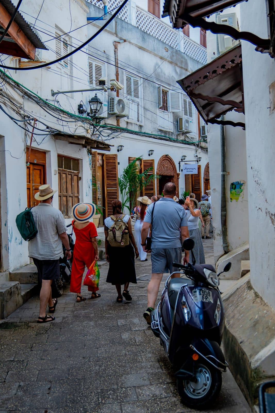 Travellers walking a narrow lane between whitewashed buildings in Stone Town